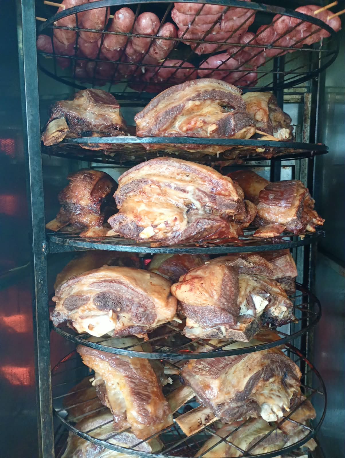 Costelas bovinas e linguiças assando no forno giratório
